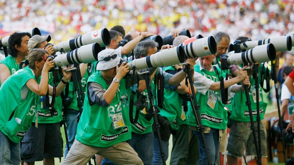fotografer yang memotret pertandingan di dalam stadion selain membawa kamera tapi juga lensa-lensa kamera yang menunjang dan biasanya merupakan lensa yang mempunyai zoom yang oke seperti lensa-lensa telefoto.